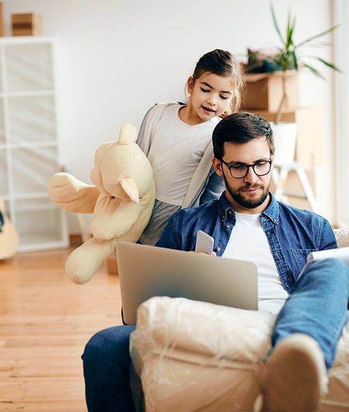 Father working on a laptop while his daughter plays beside him
